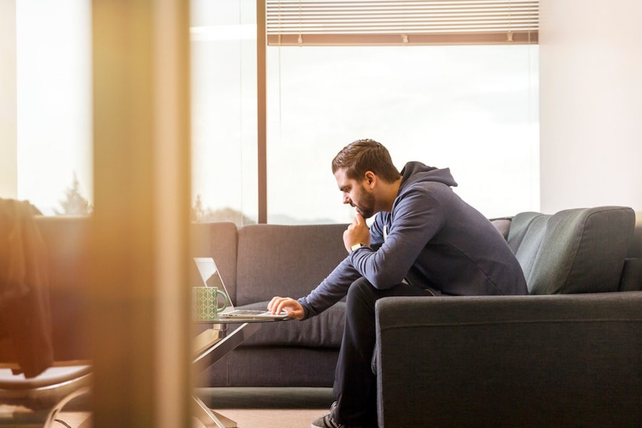 A man sitting on a couch and working on his laptop.